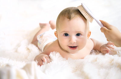 Mother brushing hair of cute baby lying on bed at home