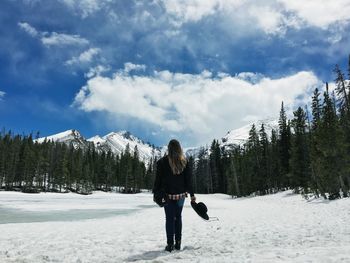 Rear view of woman standing on snow covered field against trees