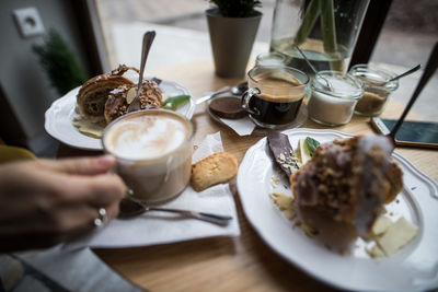 Cropped hand with coffee and dessert on table