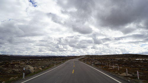 Road leading towards mountains against cloudy sky