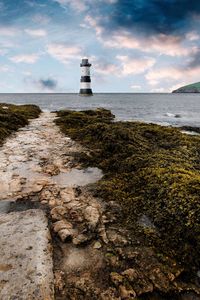 Lighthouse on beach by sea against sky