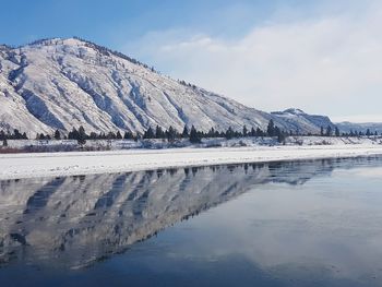 Frozen lake by snowcapped mountain against sky