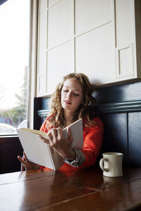 Woman reading book while sitting by window in cafe