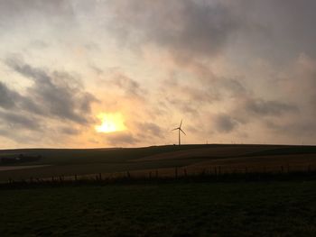 Silhouette of windmill on field against cloudy sky