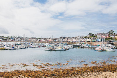 Sailboats moored in harbor by buildings against sky