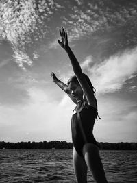 Full length of woman with arms raised in sea against sky