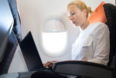 Side view of businesswoman working on laptop sitting at airplane