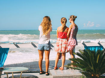 Rear view of women standing at beach against sky