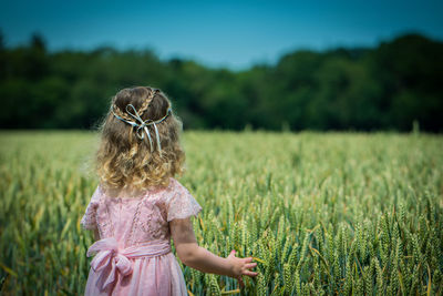 Rear view of girl standing by crops on agricultural field