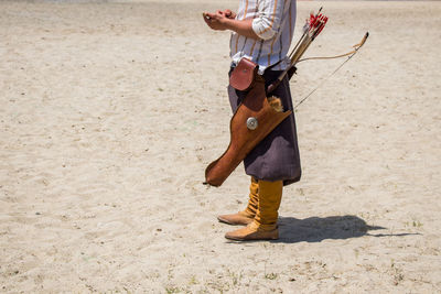 Low section of man with bow and arrow standing on sand