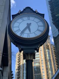 Low angle view of clock on street amidst buildings in city