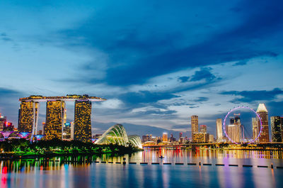 Illuminated city by river against sky