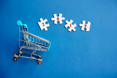 Directly above view of puzzle pieces by miniature shopping cart over blue background