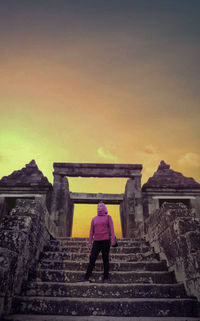 Rear view of woman standing on staircase against sky during sunset