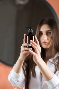 A beautiful brunette girl with long hair holds a brown dispenser with an organic cosmetic product. 