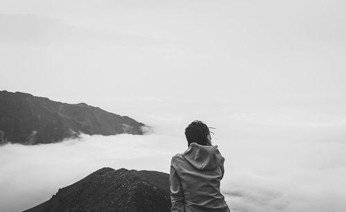 Rear view of woman sitting on cliff against sky