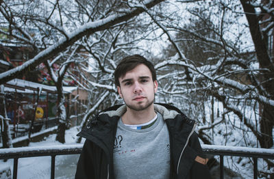 Portrait of serious young man standing by railing during winter