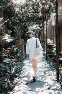 Rear view of woman walking on footpath by plants