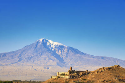 Scenic view of built structure against snowcapped mountain and sky