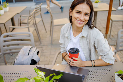 Portrait of young woman using mobile phone while sitting at cafe