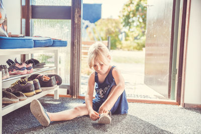 Full length of girl wearing shoe while sitting on carpet at home