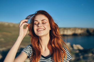 Portrait of smiling young woman using smart phone against sky