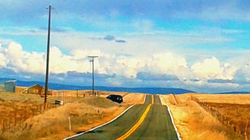 Road passing through field against cloudy sky