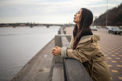 Thoughtful asian woman in coat on city bridge