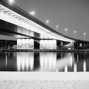 Illuminated bridge over river against sky at night