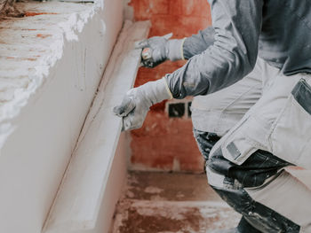 Young caucasian guy plasterer holds a wooden rule and levels a freshly puttyed wall