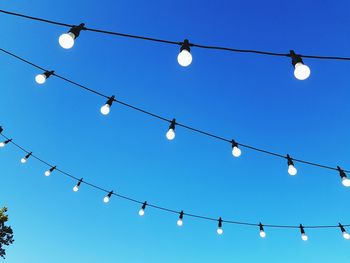 Low angle view of light bulbs hanging against blue sky