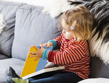 Girl reading book while sitting on sofa at home