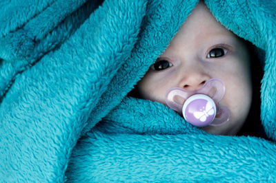 Directly above portrait of cute baby girl sucking pacifier amidst blue blanket