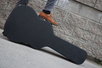 Low section of man on guitar case against wall