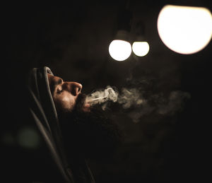Side view of mature man smoking while standing outdoors at night