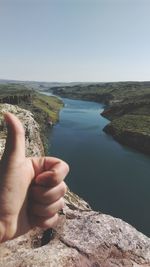 Cropped hand gesturing thumbs up against river