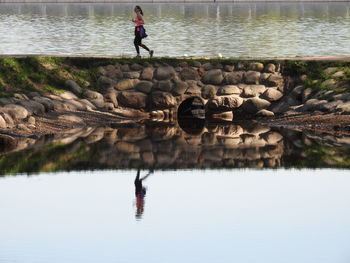 Reflection of woman running on footpath in lake