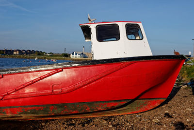 Red boat moored on beach against sky