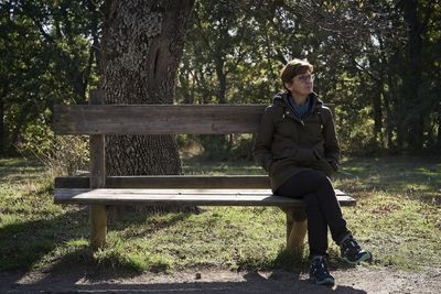 Full length of woman sitting on bench against trees at park