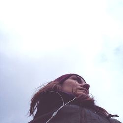 Low angle view of woman wearing headphones and looking away against sky