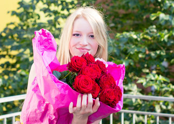 Portrait of smiling girl holding pink rose outdoors