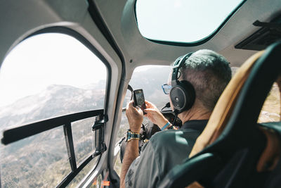 Retired man takes photo with phone from inside helicopter.