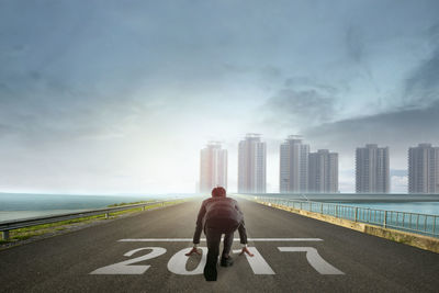 Rear view of businessman crouching on bridge over sea against sky