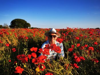 Man standing amidst red and yellow flowering plants in field against sky