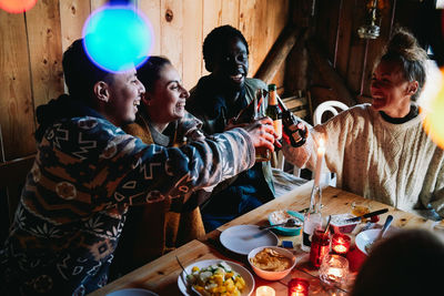 High angle view of happy male and friends toasting beer bottles in log cabin