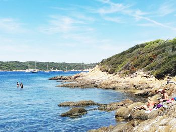 People sitting on shore by sea against blue sky