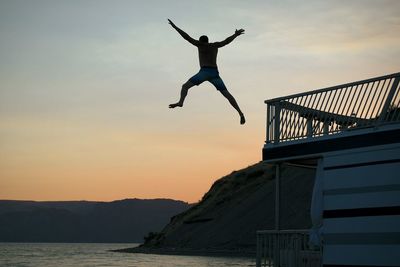 Man jumping in sea against sky during sunset