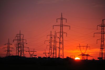 Low angle view of silhouette electricity pylons against clear sky