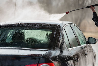 Cropped hand spraying water on car