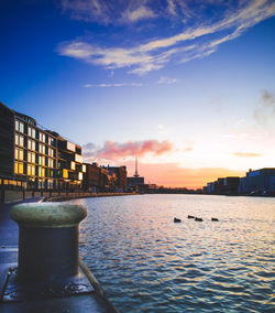 Sea by cityscape against sky during sunset